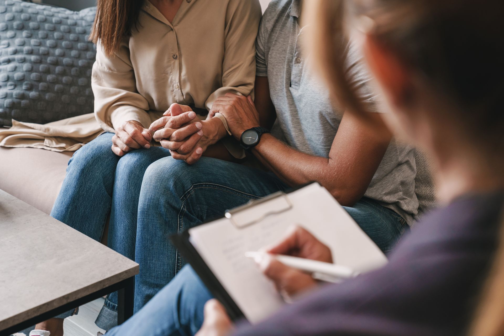 Couple holding hands during therapy session; therapist taking notes. Couple holding hands during therapy session; therapist taking notes.