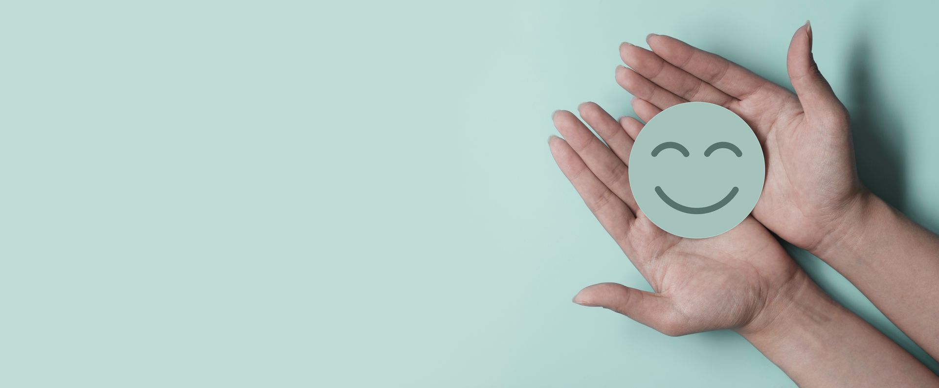 Hands holding a paper smiley face on a light blue background. Hands holding a paper smiley face on a light blue background.