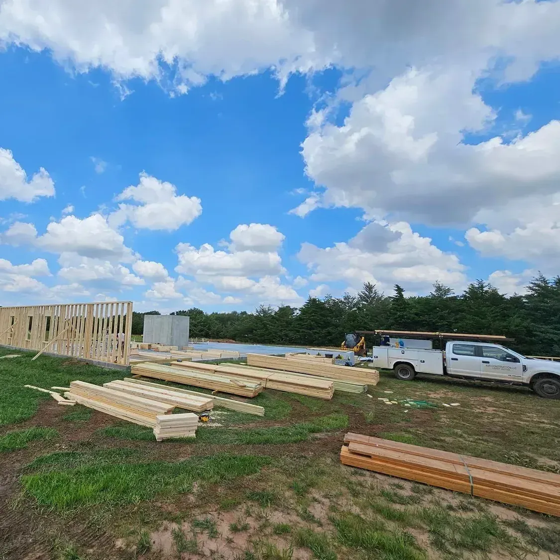 A white truck is parked in a field next to a building under construction.