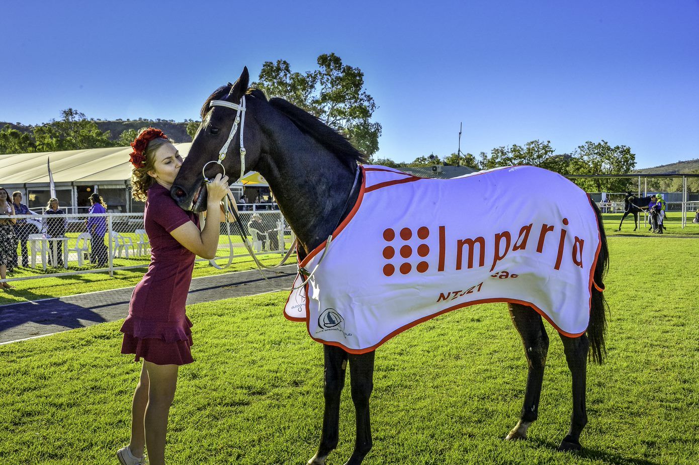 A woman is petting a horse with a blanket that says imperio on it.