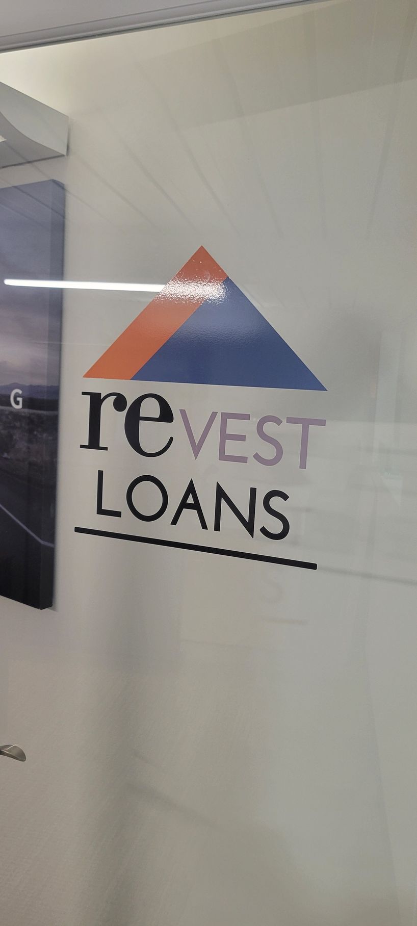 Glass wall logo reading “reVest Loans” with orange and blue triangle mark