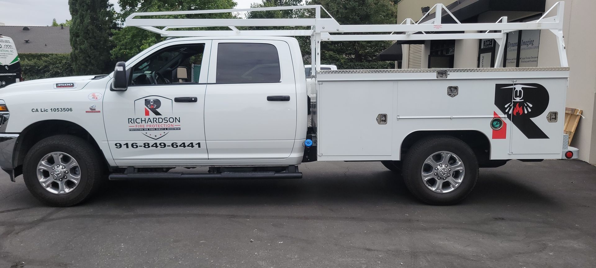 White utility truck with ladder rack and service compartments parked on a street.