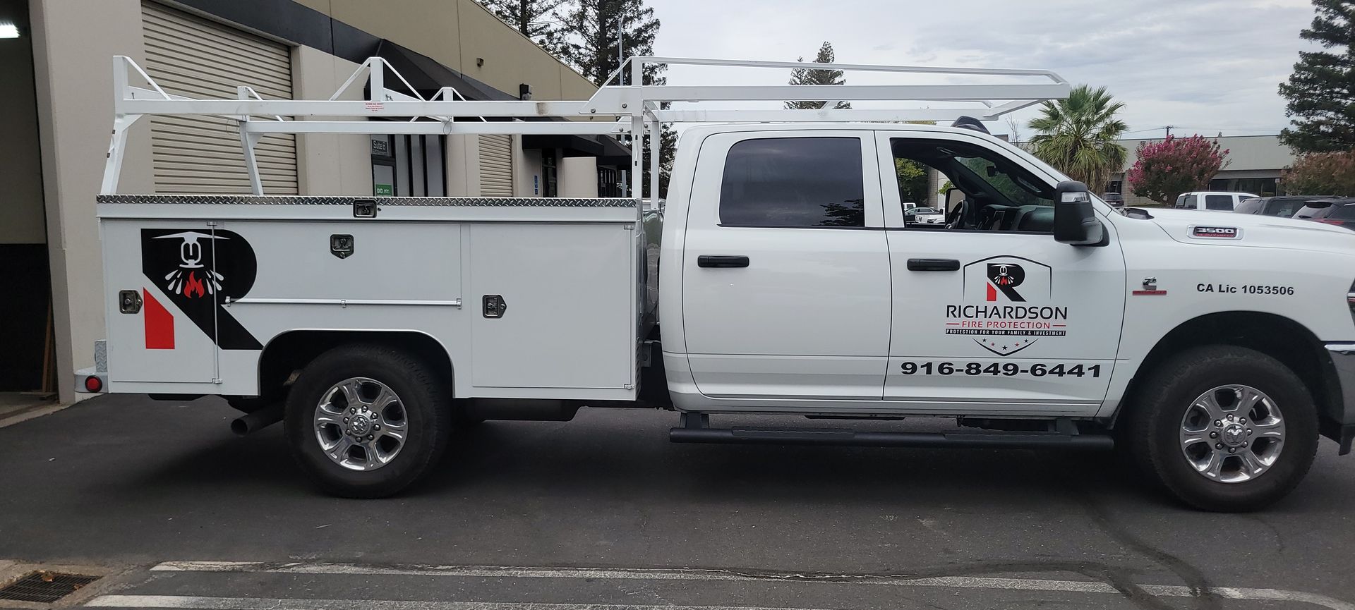 White utility truck parked on a street beside a building, with company logos and equipment compartments.