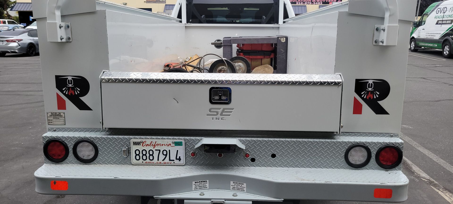Rear view of a white utility truck with red taillights and a license plate, parked on a street.