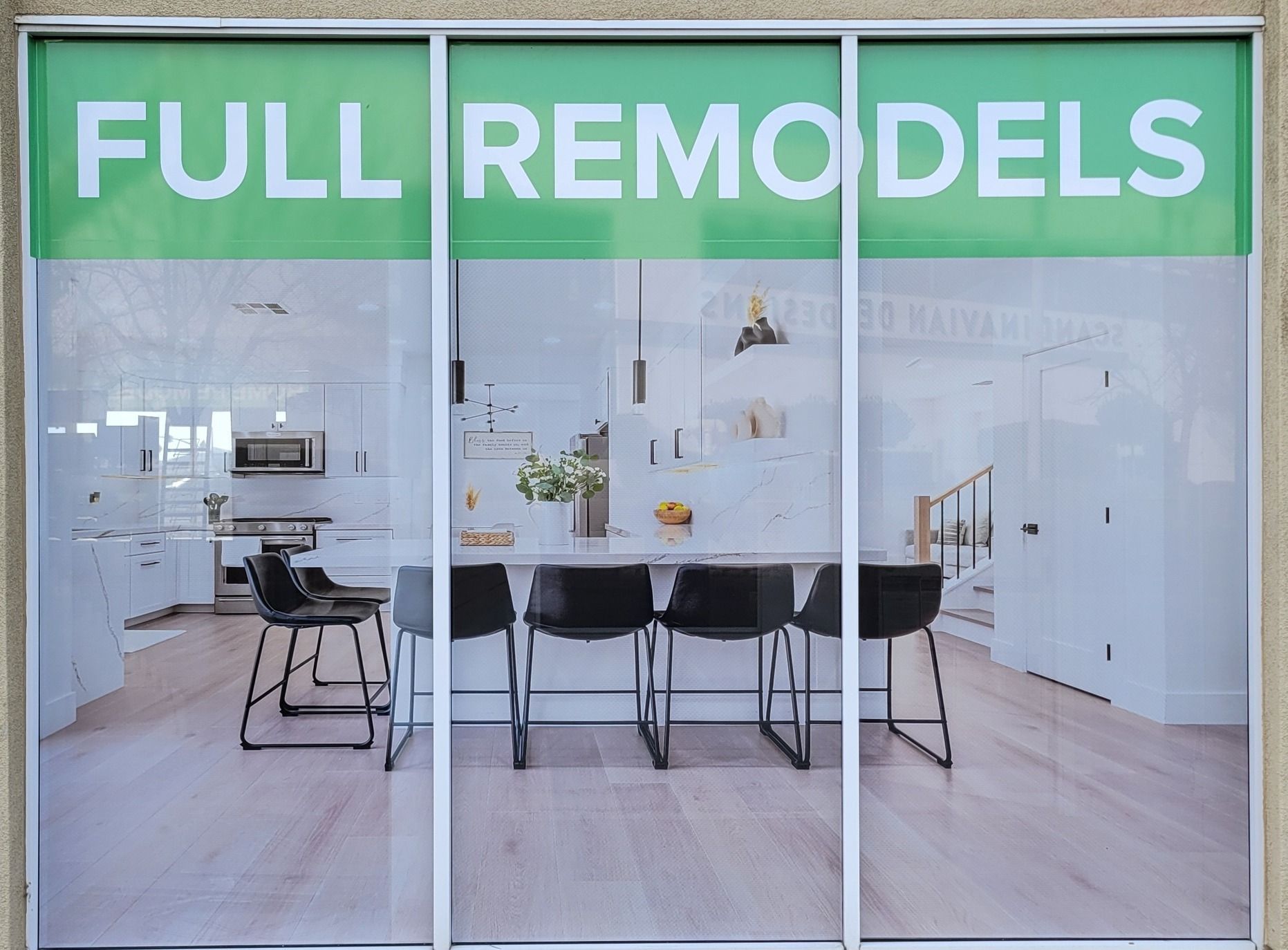Storefront with green “FULL REMODELS” sign and a modern white office interior behind glass doors