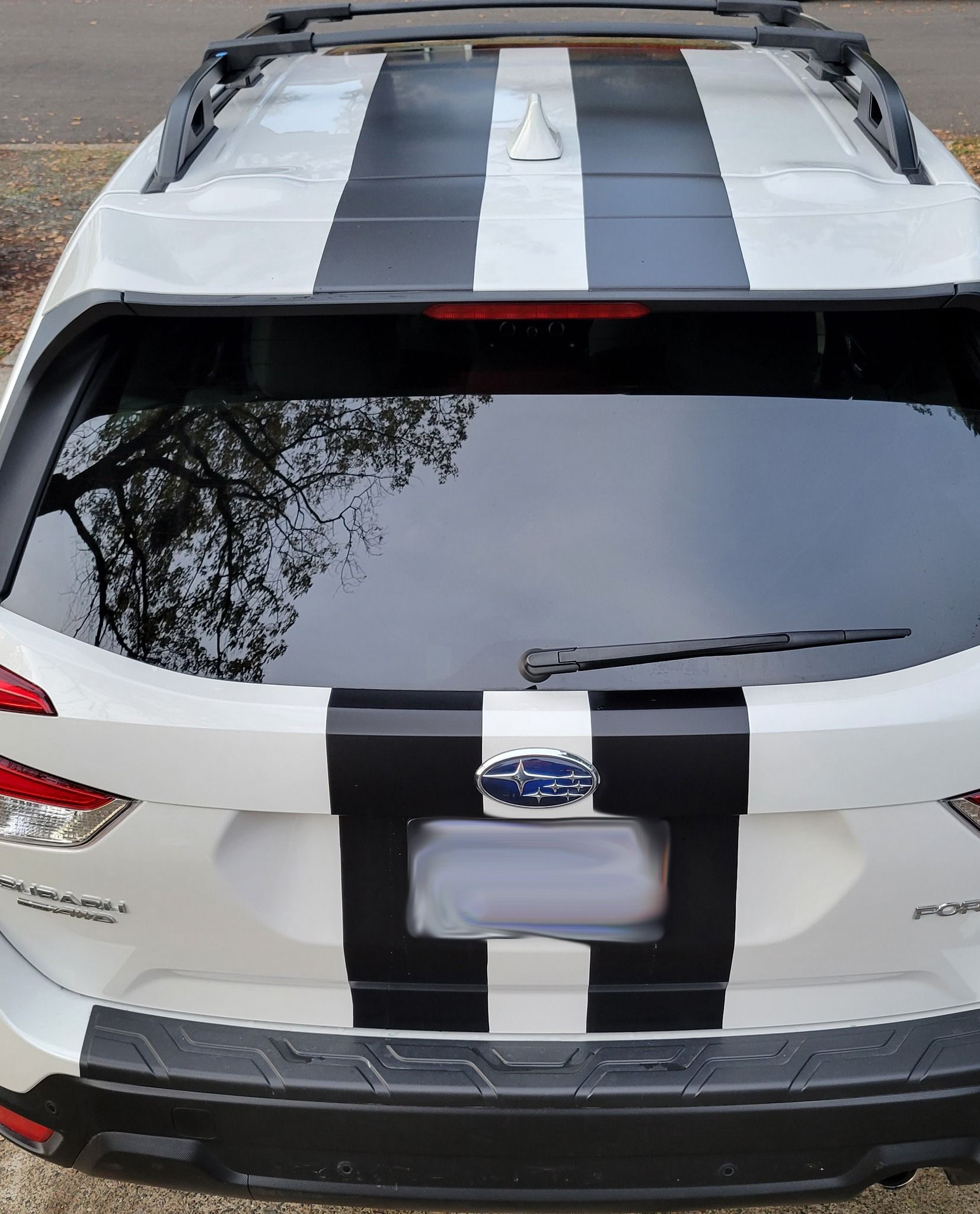 White SUV with black racing stripes parked outdoors, rear view.