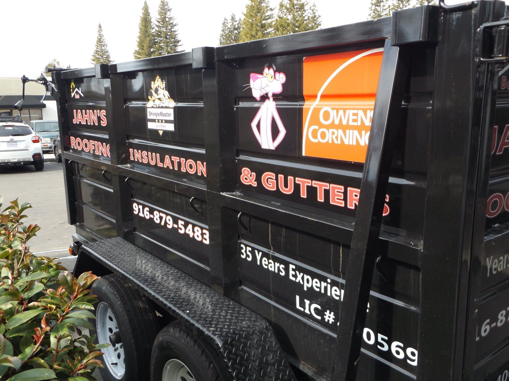 Black dump trailer with orange and white business logos, including 