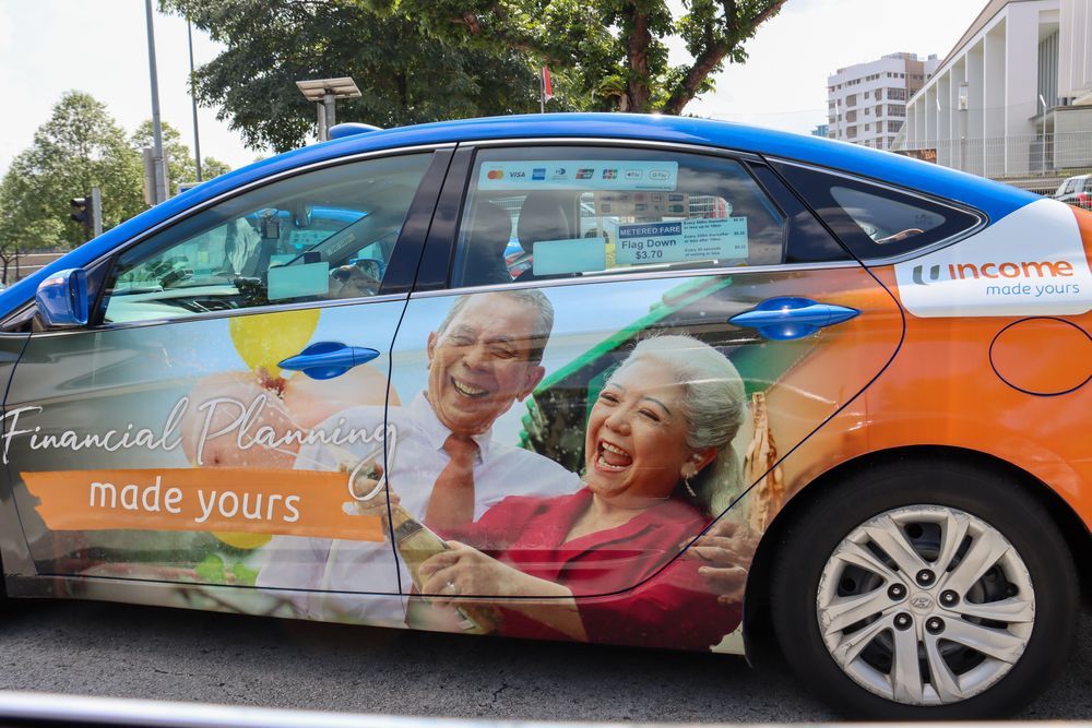 Blue and orange taxi with elderly couple smiling on side. Text reads