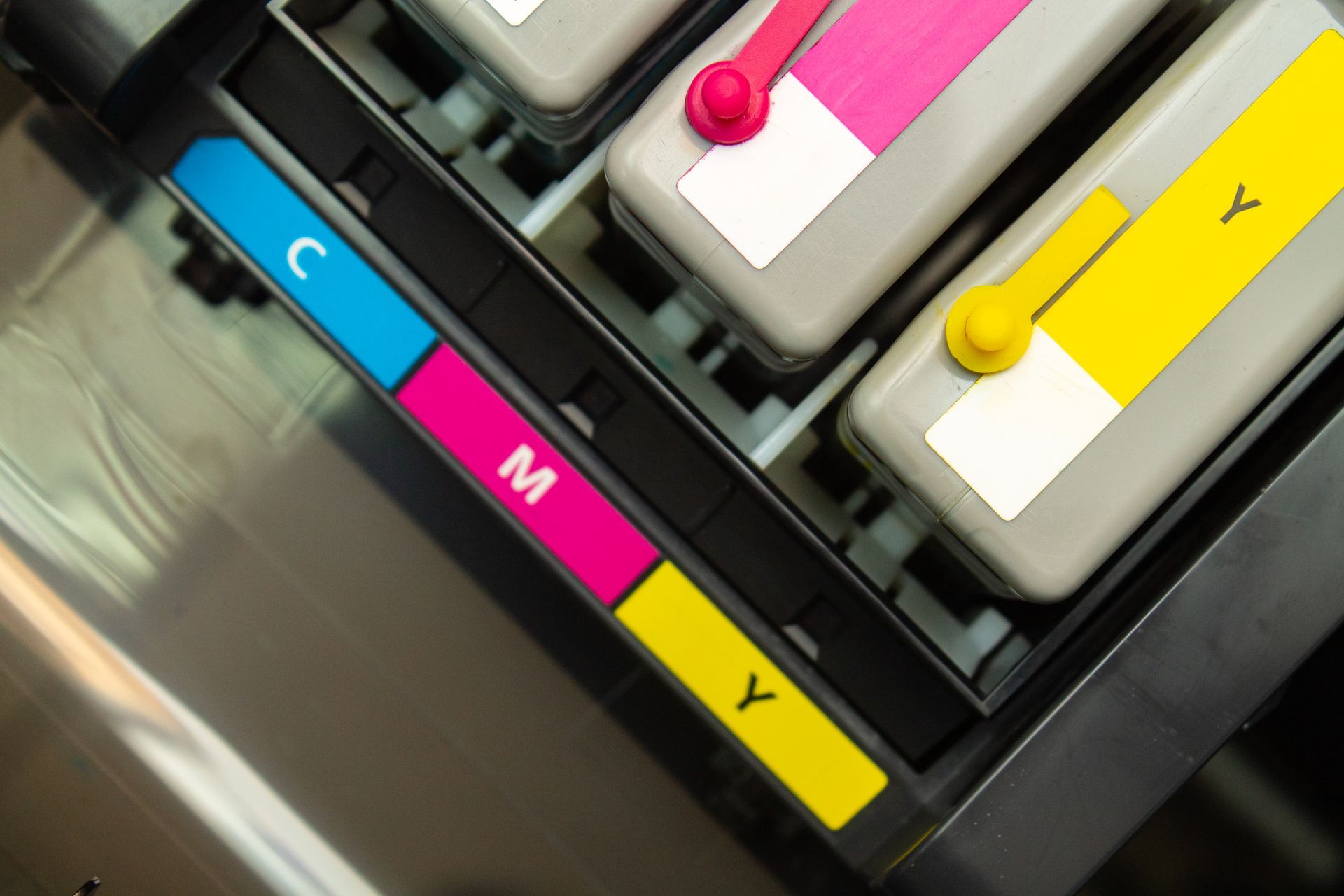 Close-up of printer ink cartridges: Cyan, Magenta, Yellow (CMY), with matching color indicators.