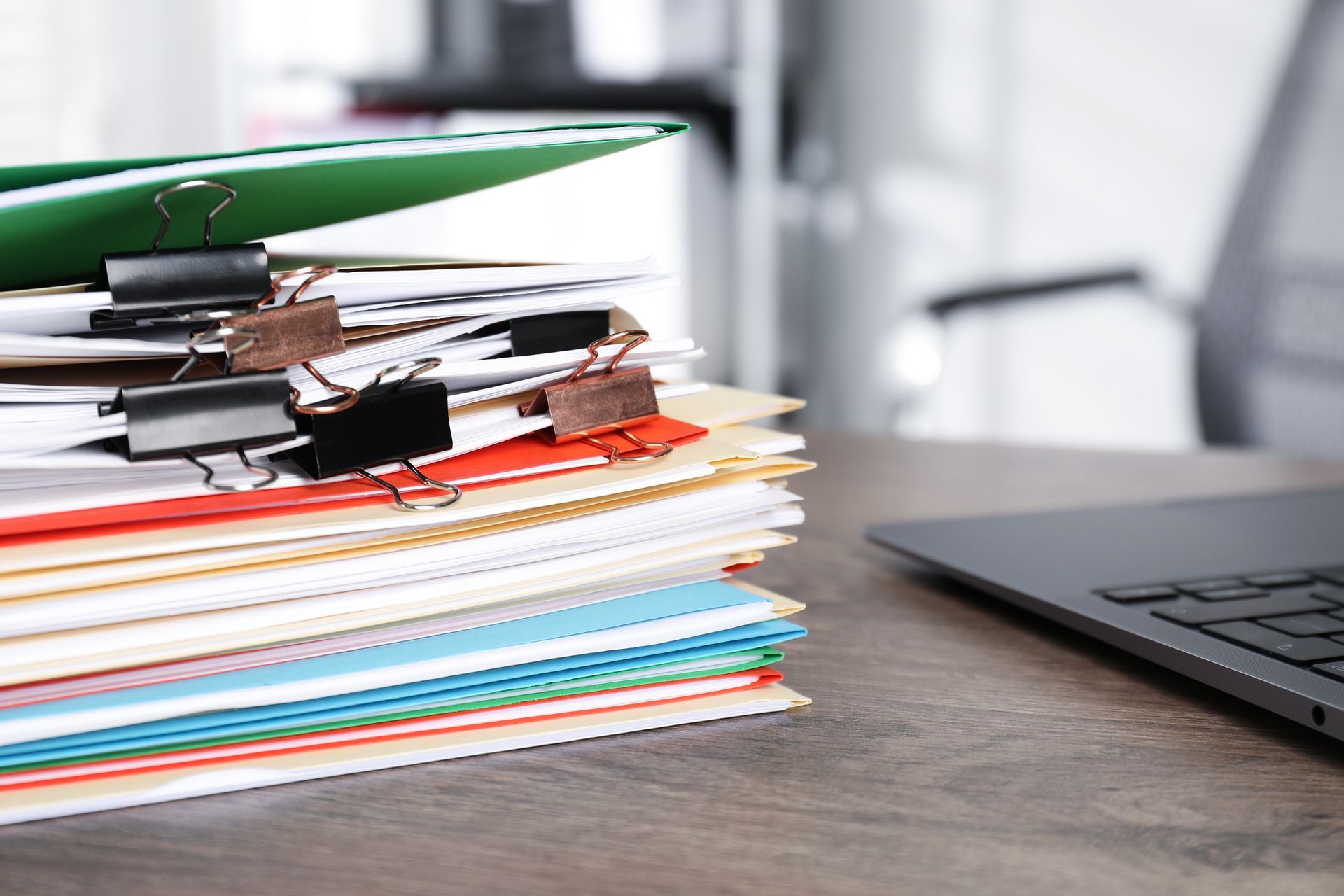 Stack of folders and papers with a laptop on a desk
