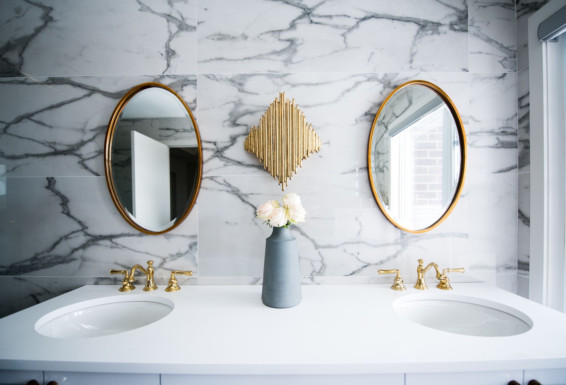 A bathroom with two sinks , two mirrors and a vase of flowers.