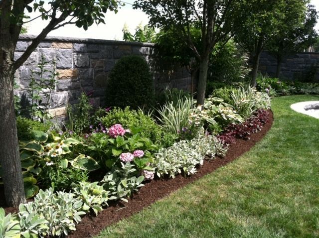 Curved flower bed with pink and white blooms beside a stone wall and green lawn