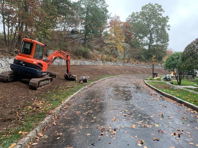Orange excavator beside wet curved road in a wooded park during autumn