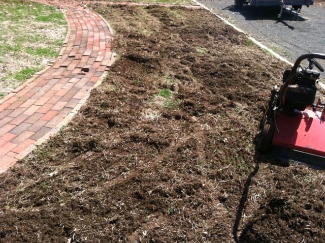 Freshly tilled soil beside a curved brick path, with a red lawn mower on the right edge.