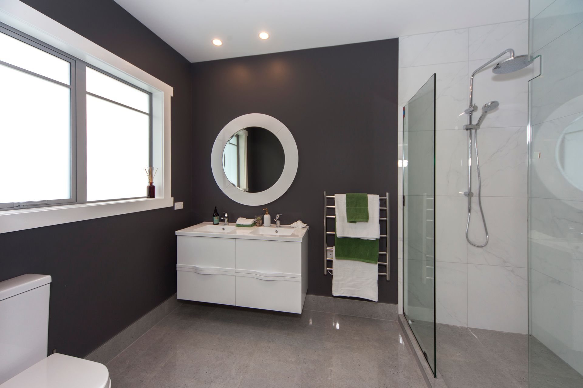 Modern bathroom with dark gray wall, white vanity, large mirror, and glass shower by Neda Builda