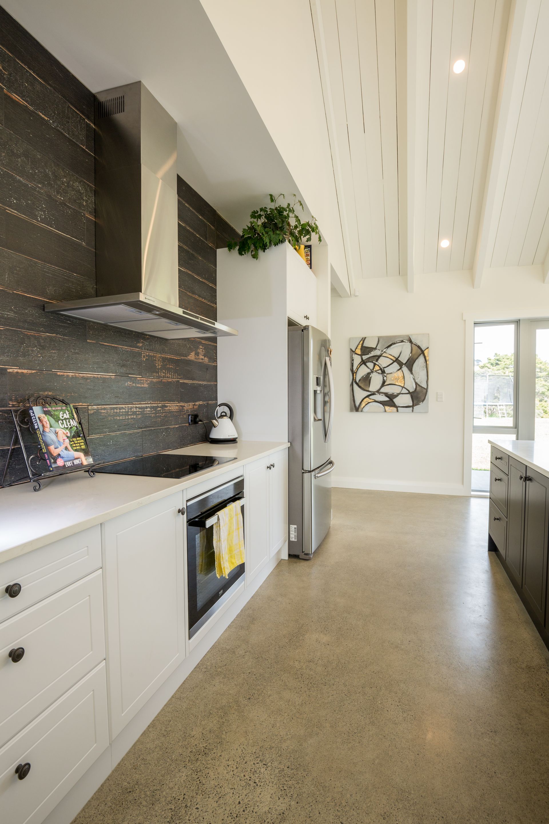 Modern kitchen with white cabinets, stainless steel appliances, and dark backsplash by Neda Builda