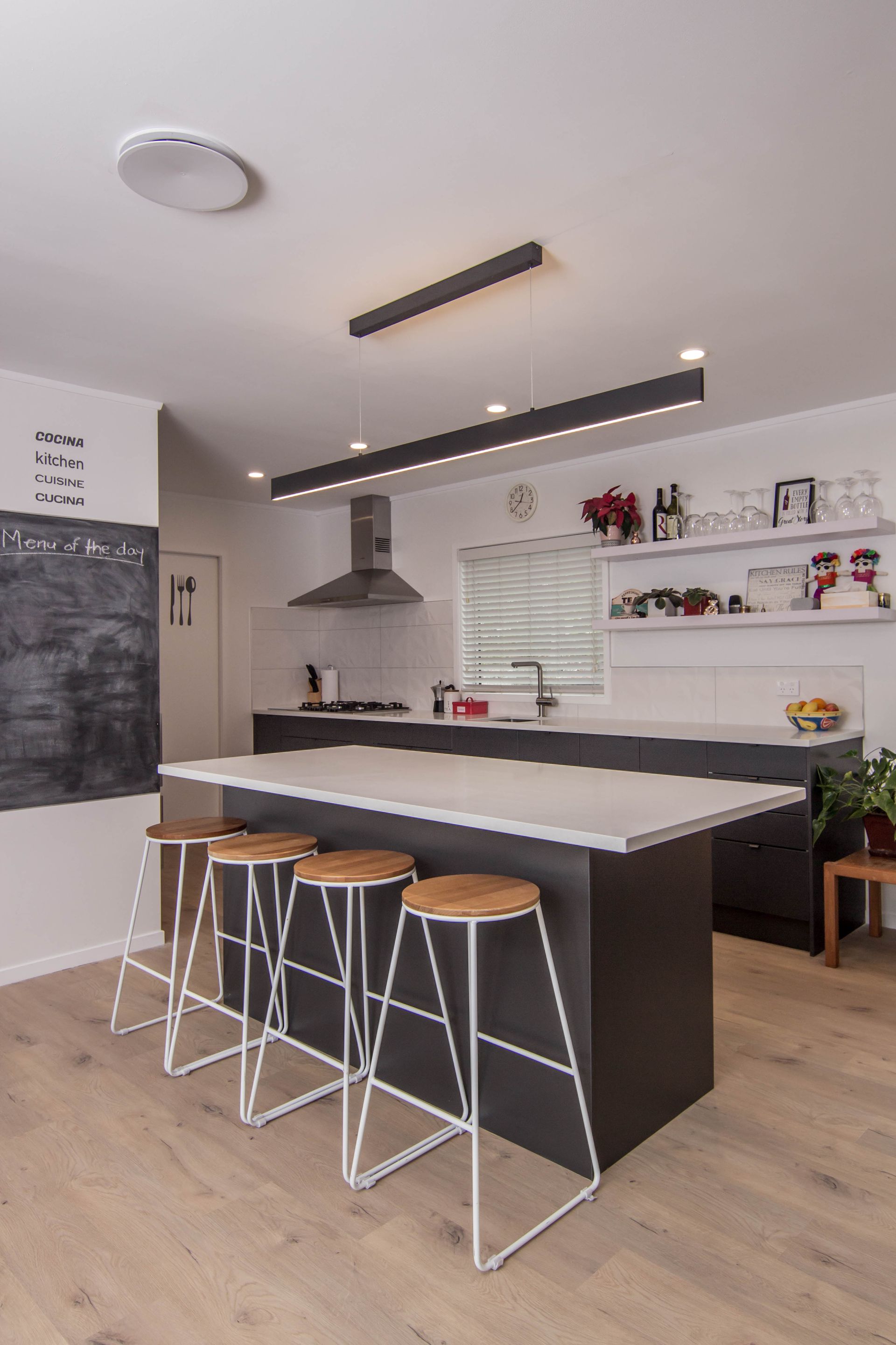 Modern kitchen with a dark island and white countertops. Wood floors and bar stools by Neda Builda