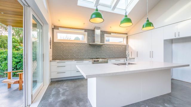 Modern white kitchen with an island, green pendant lights, and sliding glass doors by Neda Builda