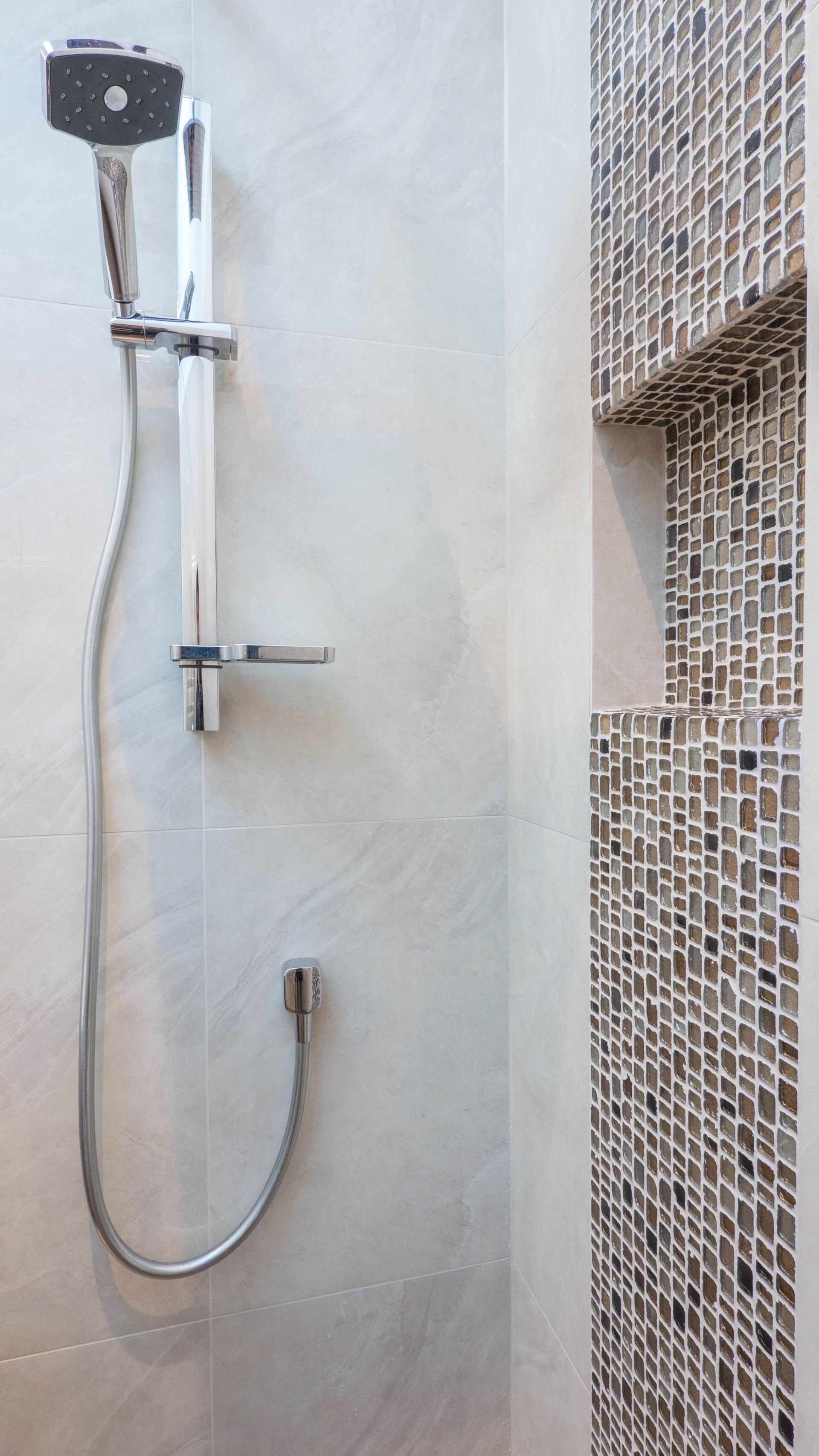Shower with adjustable chrome showerhead and built-in mosaic tile shelf by Neda Builda.