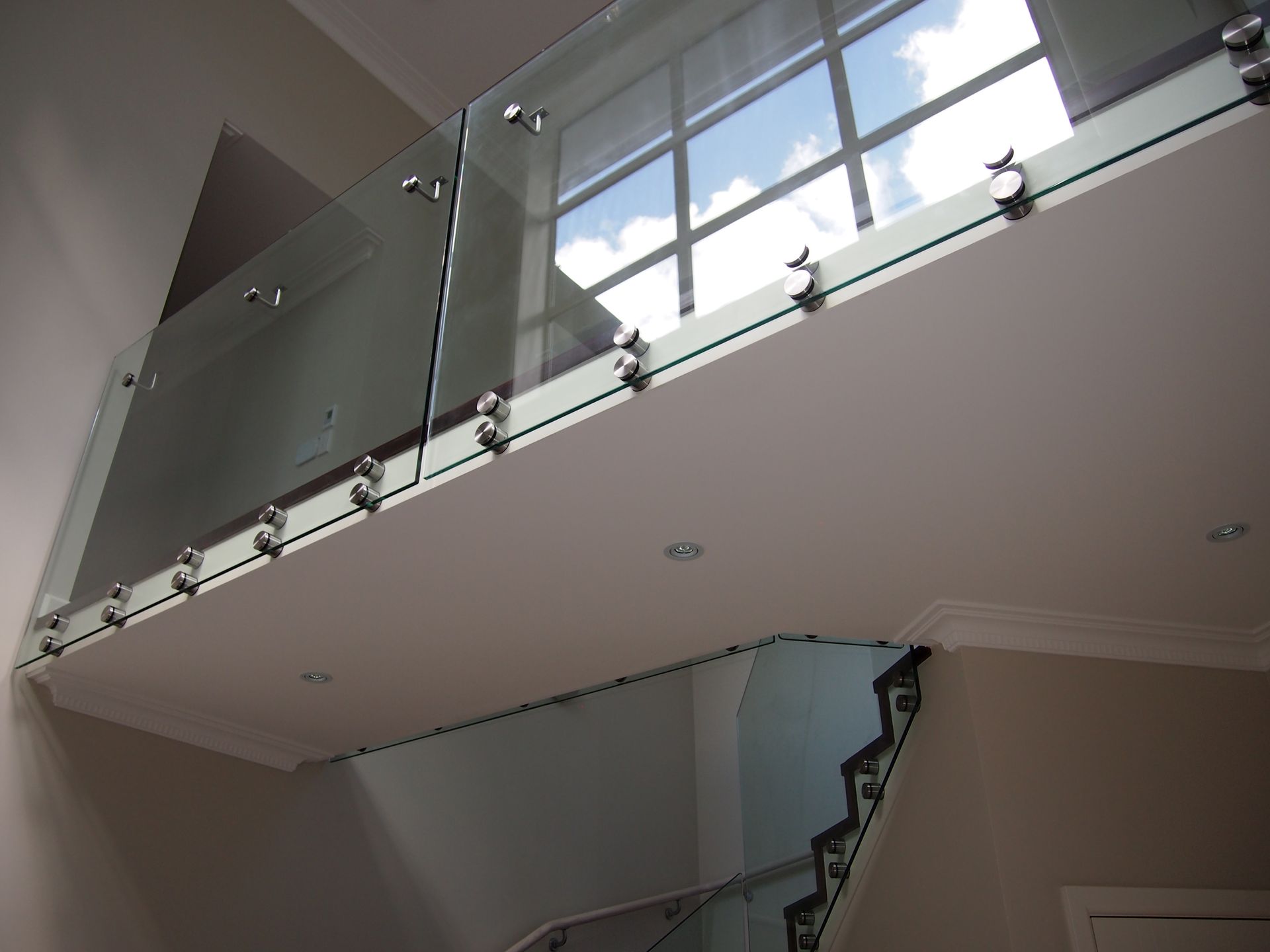Glass balcony with stainless steel hardware, overlooking a staircase and window by Neda Builda.