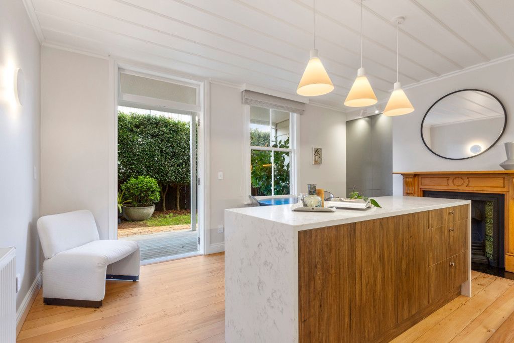 Kitchen with wooden island, open to a garden. Includes a white chair, fireplace, and pendant lights by Neda Builda.