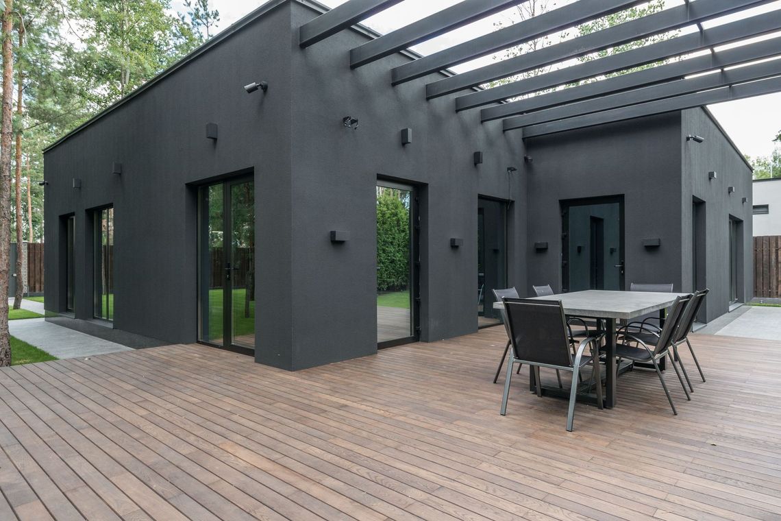 Two-story house with glass railings. Wooden stairs lead to a deck and balcony by Neda Builda