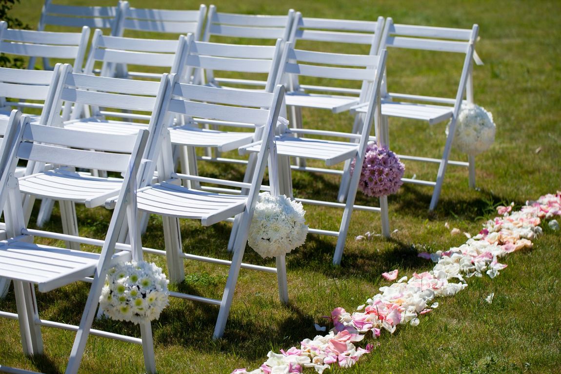 A Row of White Folding Chairs Are Lined Up in a Grassy Field