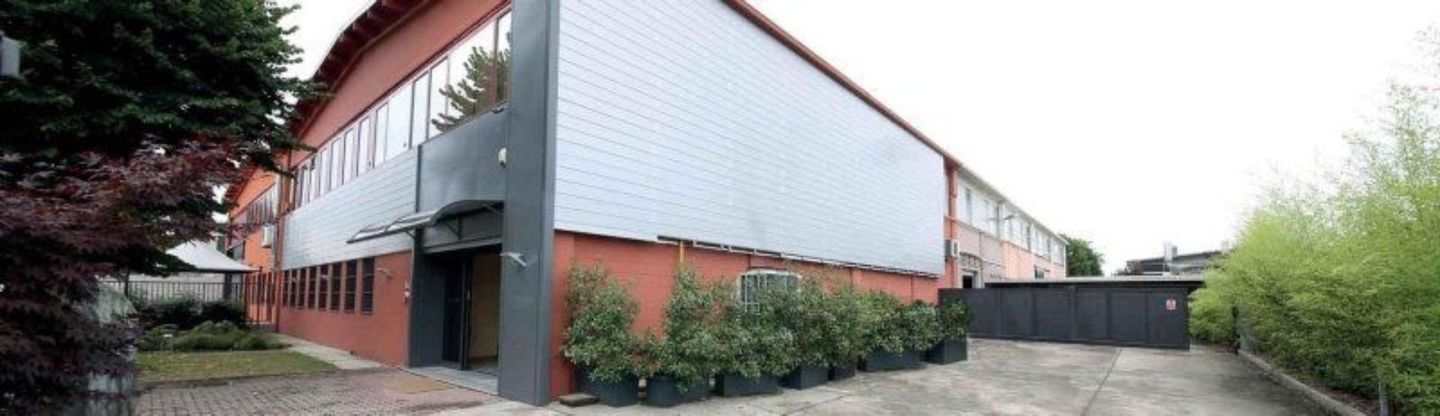 Esterno di un edificio moderno in mattoni rossi e rivestimento bianco, con un vialetto pavimentato accanto agli alberi