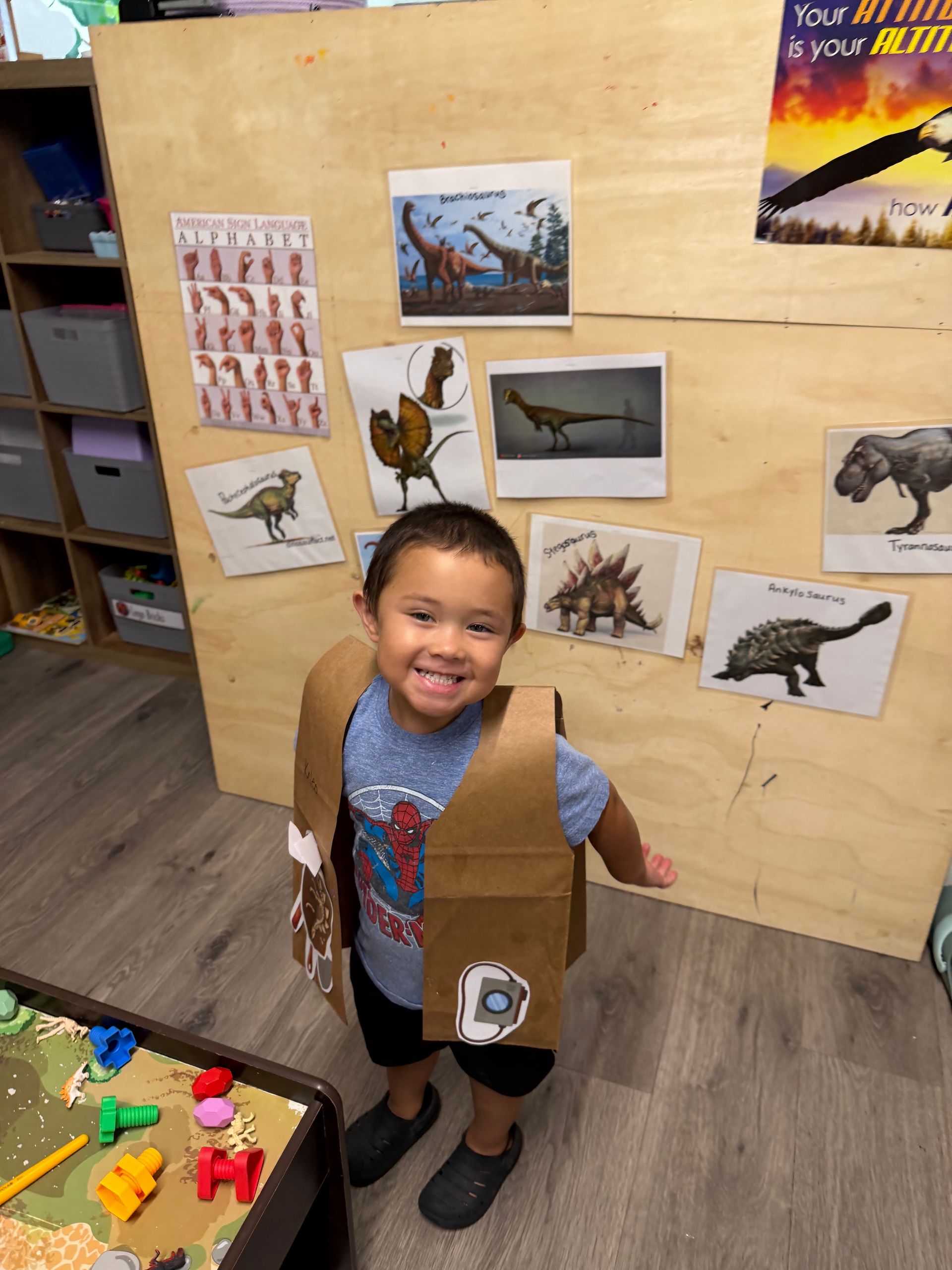 Smiling child in a classroom stands before a board with animal pictures and cutout box costume pieces