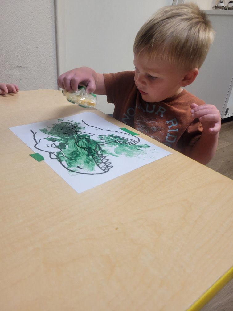 Child at a table painting on paper with green and black paint