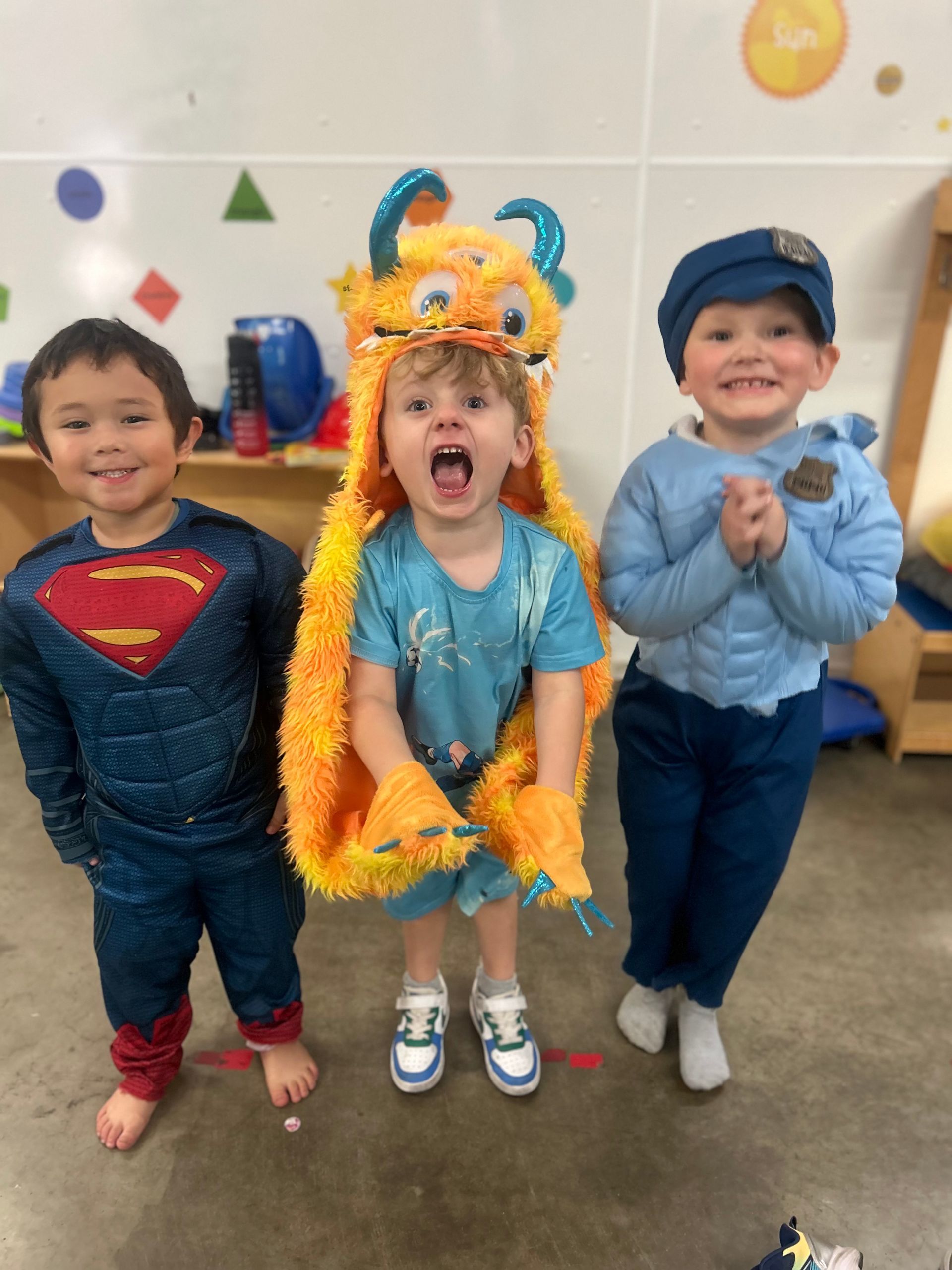 Three children in colorful costumes smile and pose indoors at a party