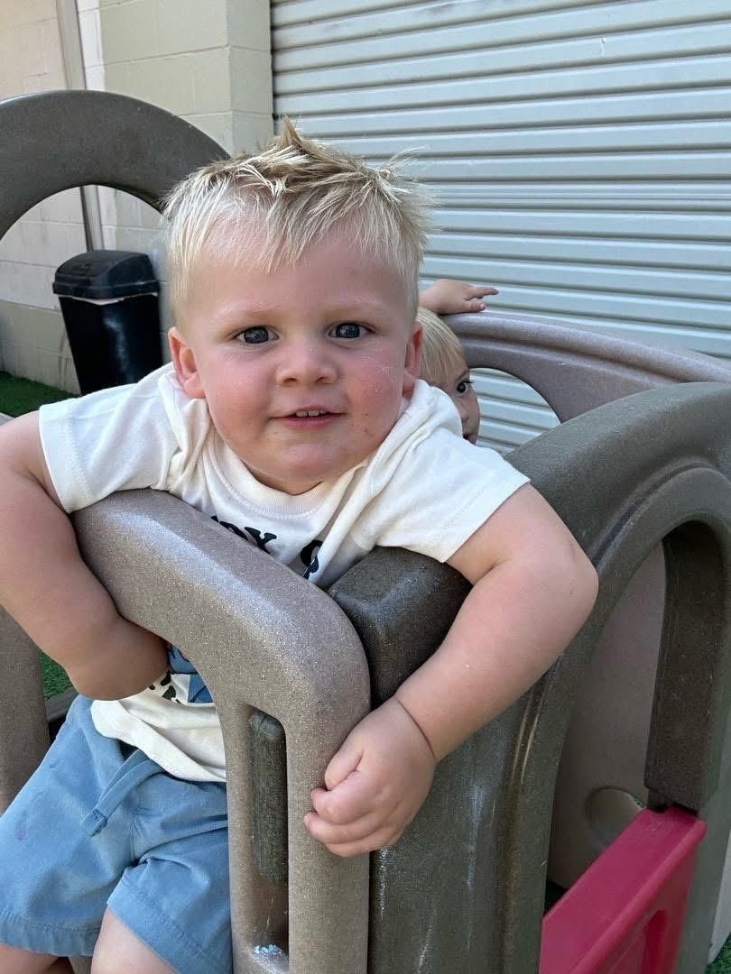 Smiling child in a white shirt and blue shorts sitting in a padded outdoor chair
