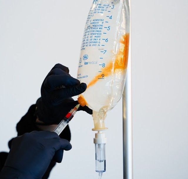 A person is holding a syringe next to an IV bag