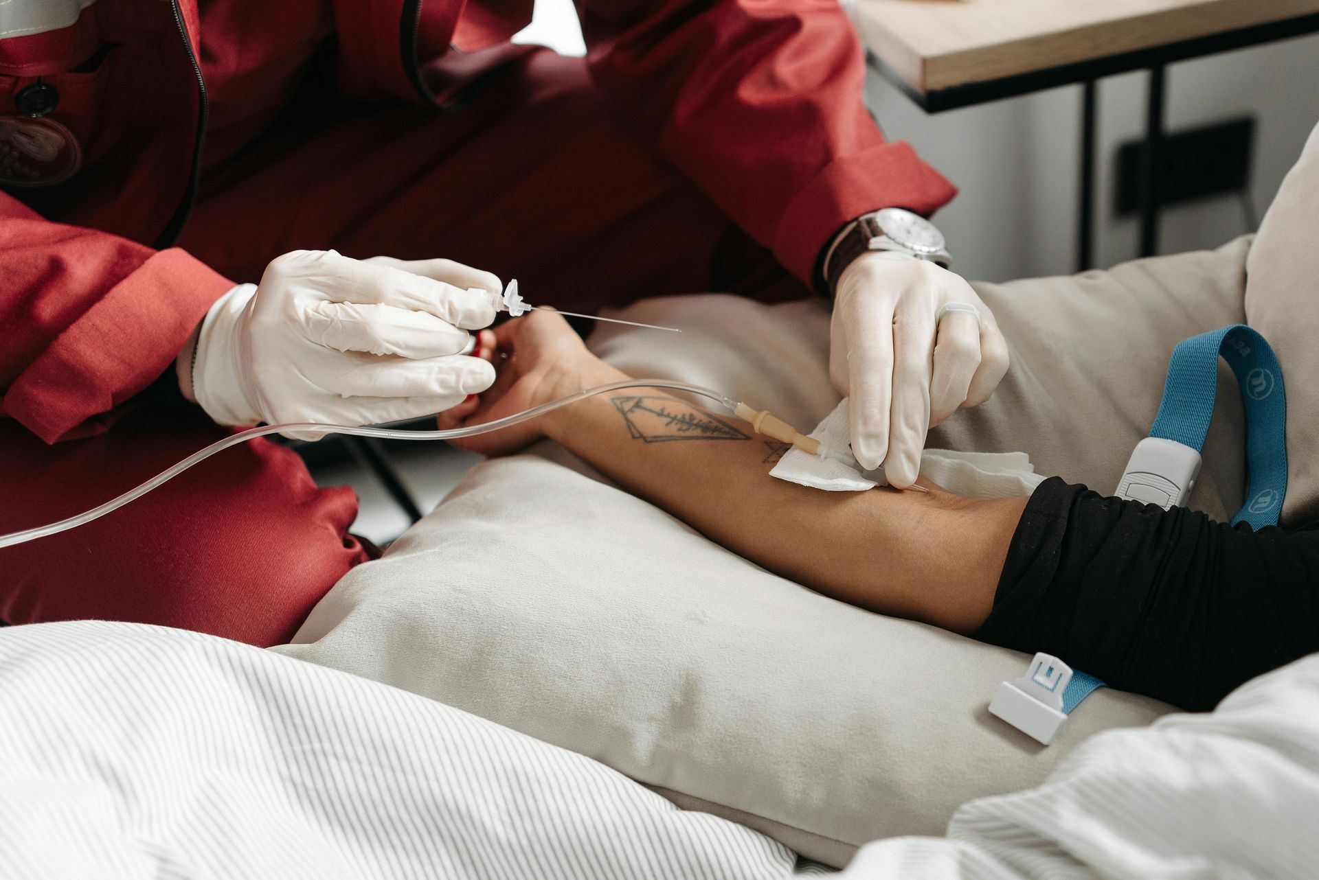 Person receiving IV therapy, medical professional adjusting the drip in indoor setting.