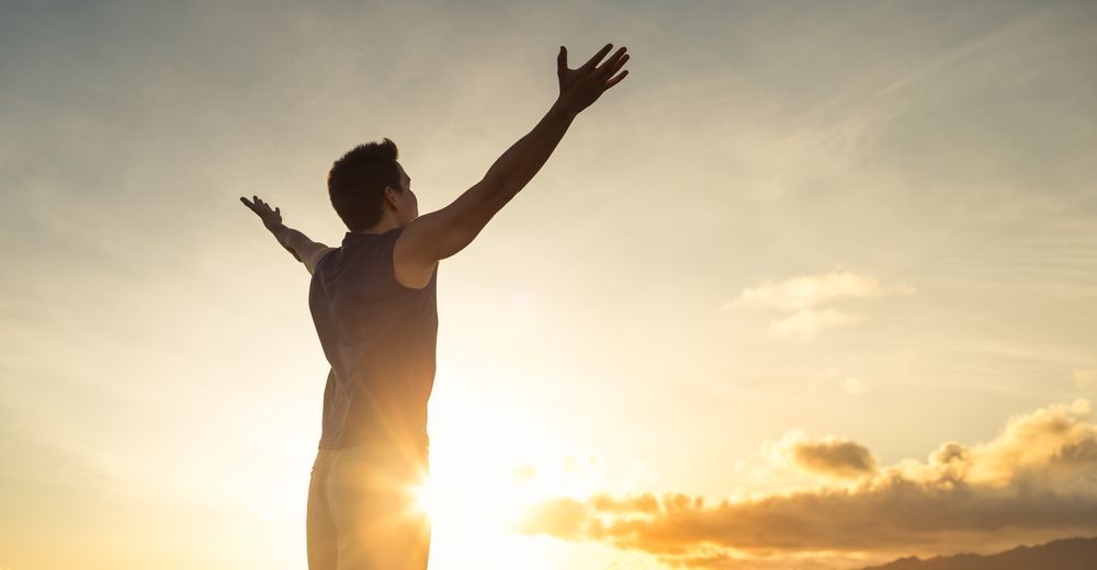 A man is standing with his arms outstretched at sunset.