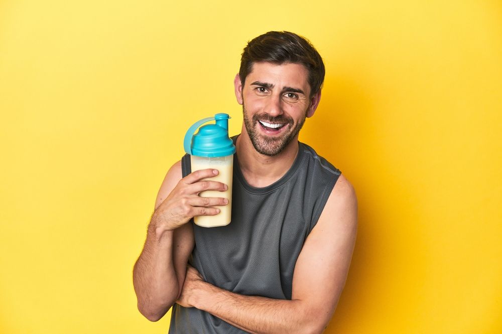 A man is holding a bottle of protein shake on a yellow background.