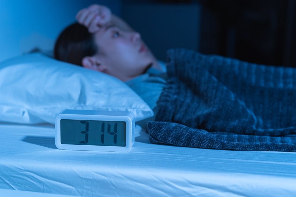 A man is sleeping in a bed next to an alarm clock.