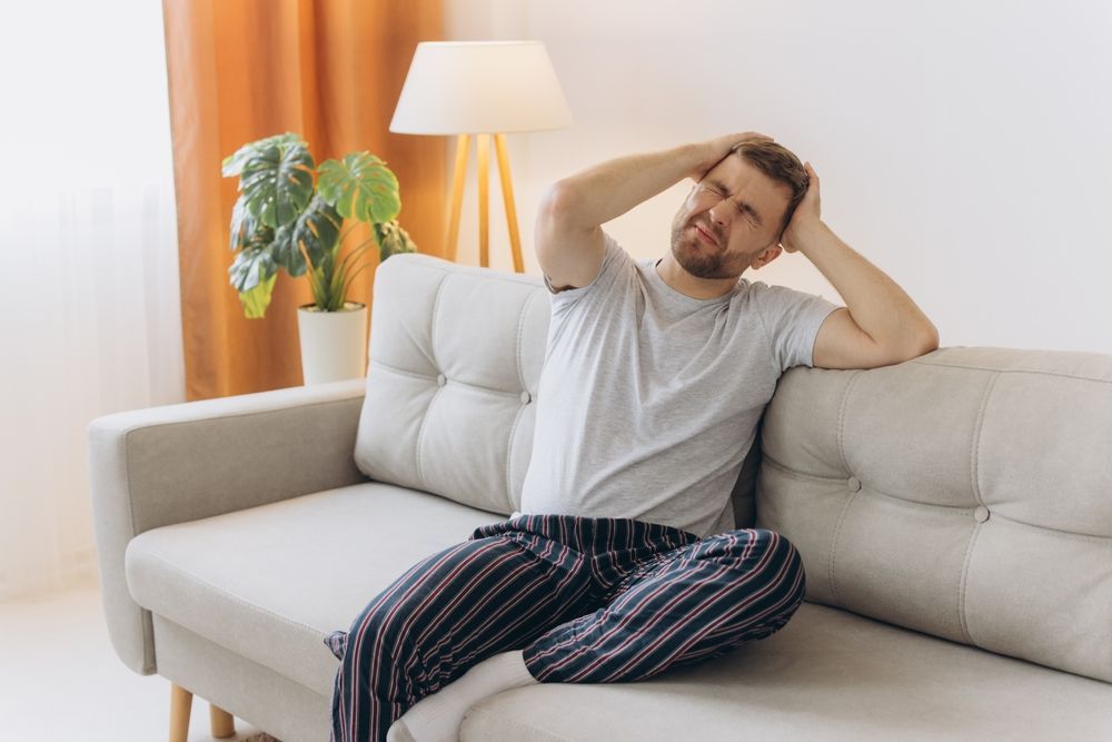 A man is sitting on a couch with his hands on his head.