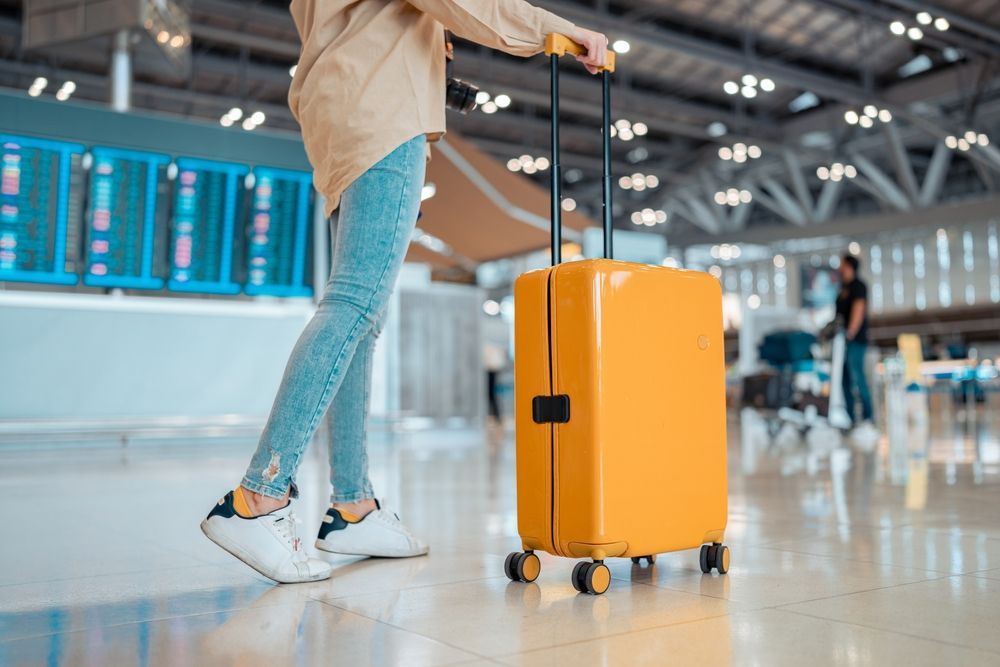A woman is walking with a yellow suitcase in an airport.
