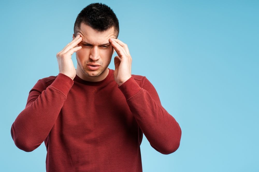 A man in a red sweater is holding his head in pain.