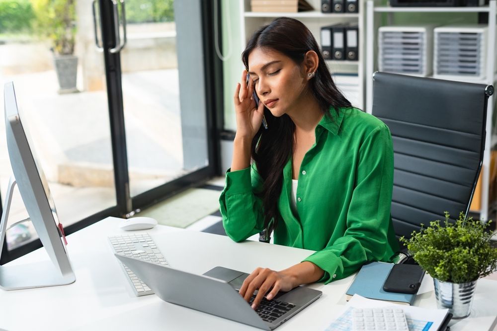 A woman in a green shirt is sitting at a desk using a laptop computer.