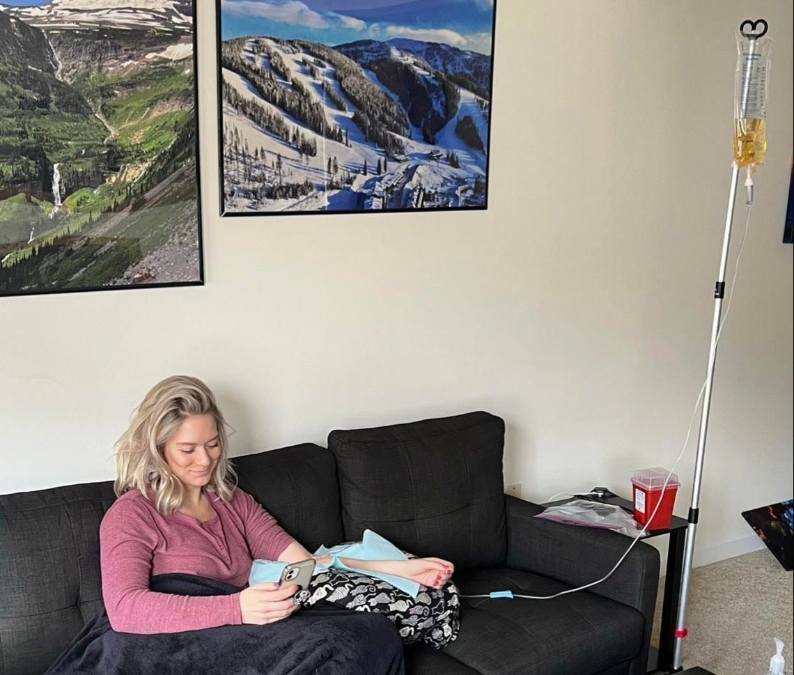 A woman is sitting on a couch with an iv in her hand.