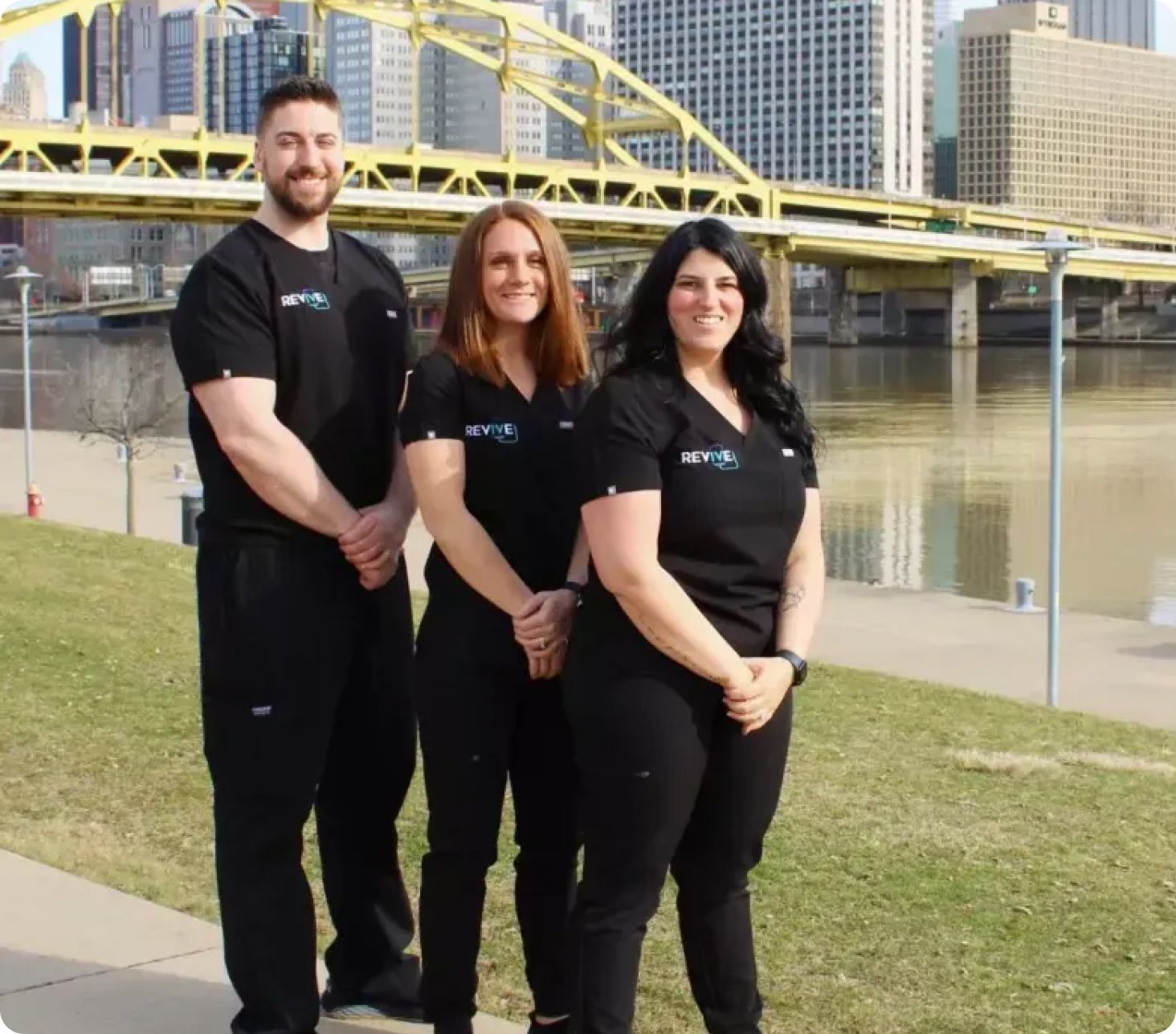 Three people are posing for a picture in front of a bridge