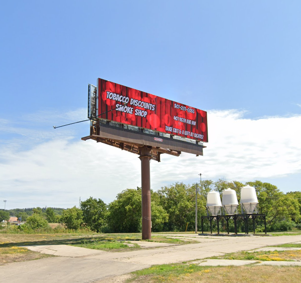Billboard advertising a smoke shop, red background, blue sky, three silos.