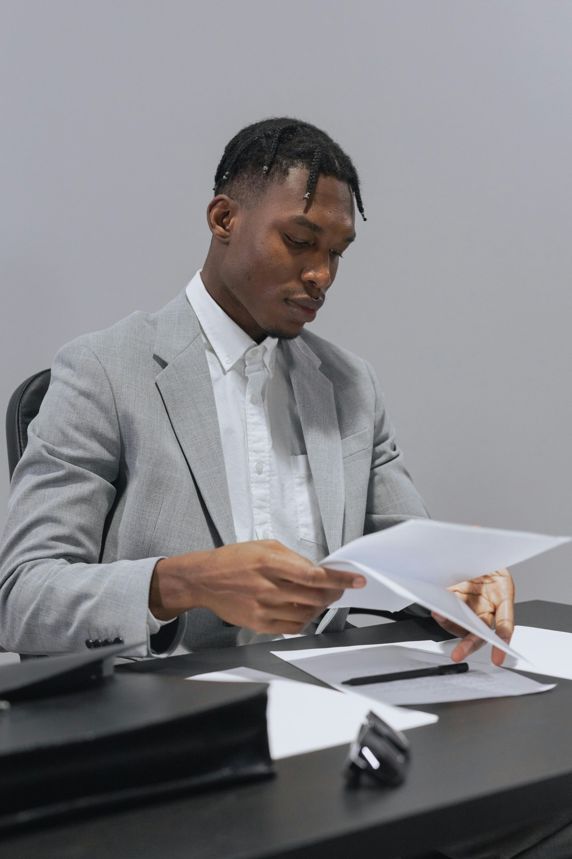Man in gray suit reviews paperwork at a desk.