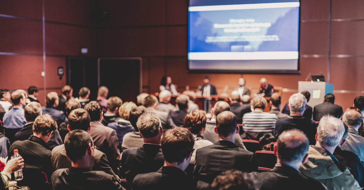 people sitting down in chairs looking at others talking on a stage