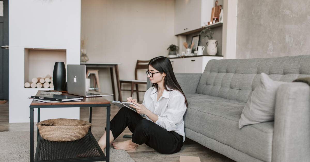 A remote worker sitting on the floor of her living room with a laptop at bridge space trying to focus in a nice environment