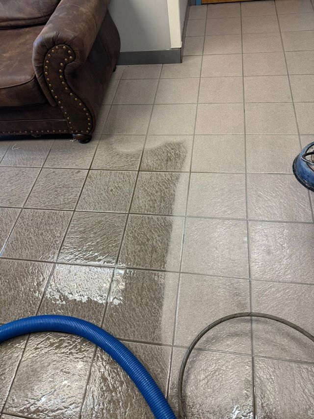 Wet tiled floor beside brown couch and blue hose in an indoor room