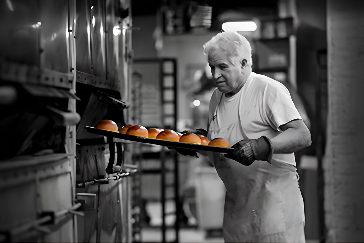 A man is holding a tray of bread in a bakery.