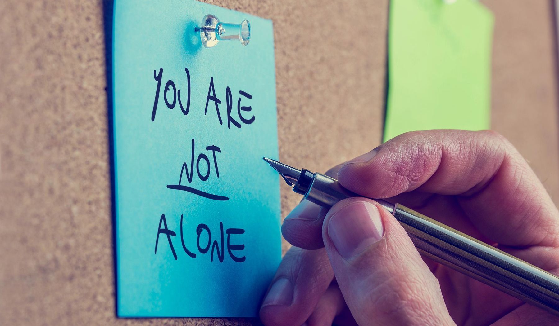 A person is writing on a sticky note that says `` you are not alone ''.